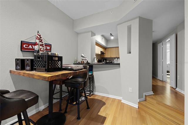 bar featuring light brown cabinets, light hardwood / wood-style flooring, and exhaust hood