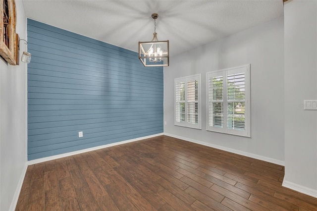 unfurnished room with a textured ceiling, dark hardwood / wood-style flooring, wooden walls, and an inviting chandelier