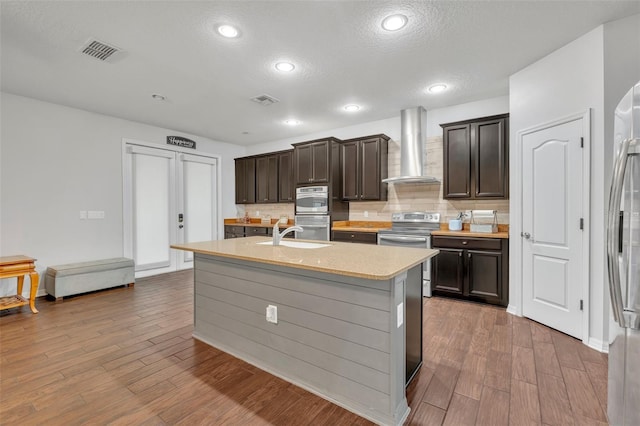 kitchen with light hardwood / wood-style floors, a textured ceiling, wall chimney range hood, and appliances with stainless steel finishes