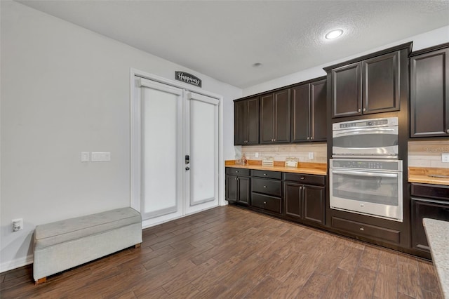 kitchen with stainless steel double oven, dark brown cabinets, dark hardwood / wood-style floors, and a textured ceiling