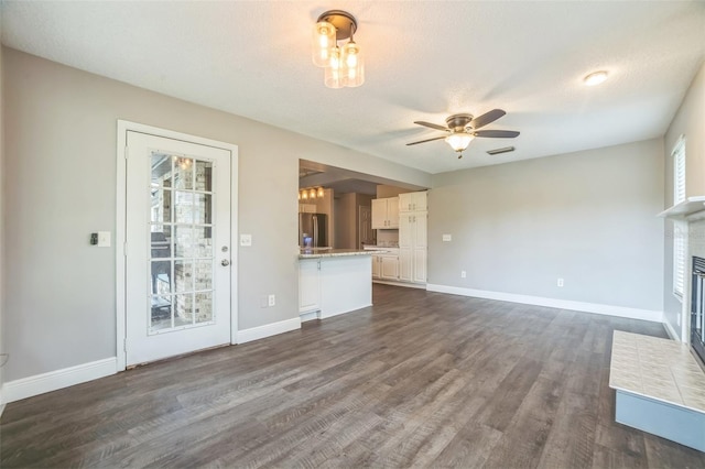 unfurnished living room with a textured ceiling, a brick fireplace, ceiling fan, and dark hardwood / wood-style flooring