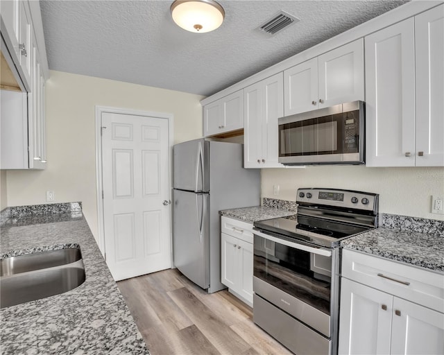 kitchen with light stone counters, light hardwood / wood-style floors, stainless steel appliances, and white cabinets