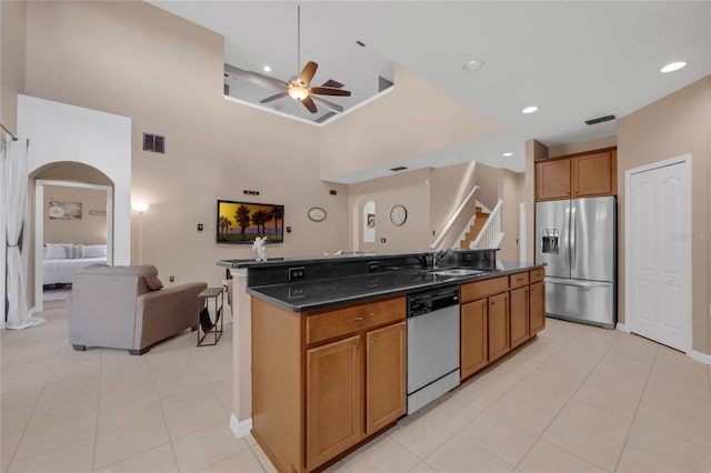 kitchen with ceiling fan, an island with sink, sink, stainless steel appliances, and a high ceiling