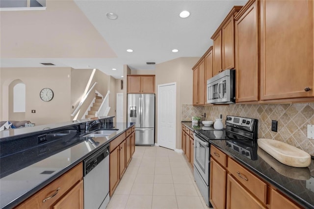 kitchen featuring light tile patterned floors, tasteful backsplash, appliances with stainless steel finishes, a sink, and dark stone counters