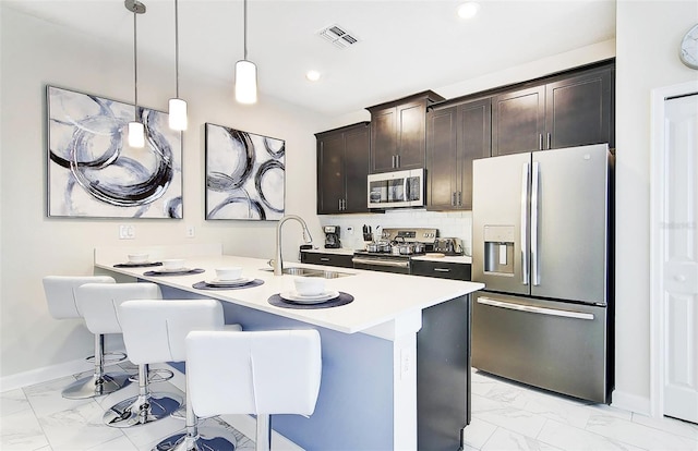 kitchen with dark brown cabinetry, sink, hanging light fixtures, appliances with stainless steel finishes, and a kitchen bar