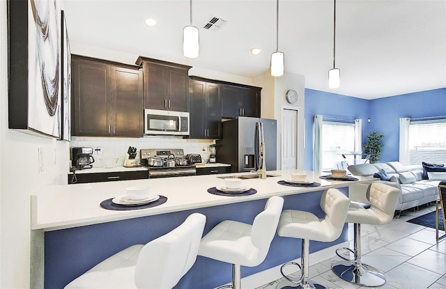 kitchen with appliances with stainless steel finishes, hanging light fixtures, a kitchen bar, and tasteful backsplash