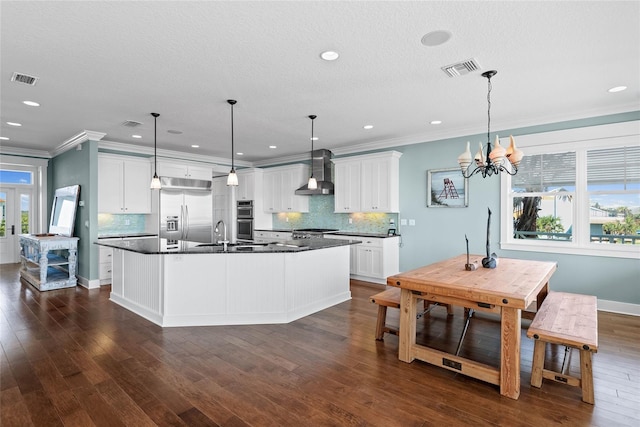 kitchen featuring wall chimney exhaust hood, appliances with stainless steel finishes, pendant lighting, and white cabinets