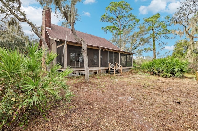 back of property with a shingled roof, a sunroom, and a chimney