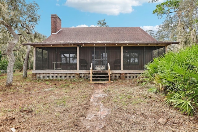 back of house with a sunroom, a chimney, and a shingled roof