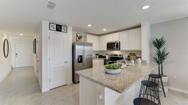 kitchen with light stone counters, white cabinets, kitchen peninsula, appliances with stainless steel finishes, and a kitchen breakfast bar