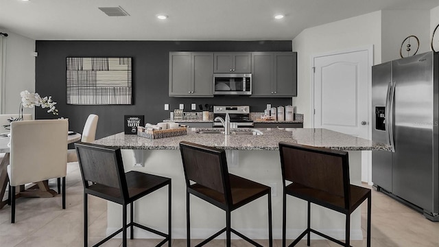 kitchen featuring light stone counters, sink, a center island with sink, gray cabinets, and appliances with stainless steel finishes