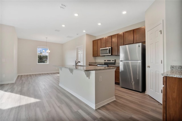 kitchen with a breakfast bar area, light hardwood / wood-style flooring, stainless steel appliances, and pendant lighting