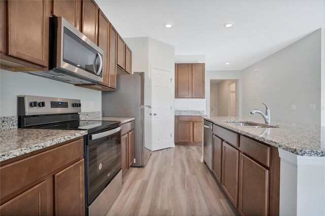 kitchen with sink, an island with sink, light hardwood / wood-style floors, stainless steel appliances, and light stone counters