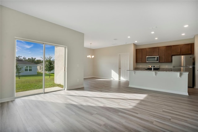 kitchen with a breakfast bar, light stone countertops, light wood-type flooring, pendant lighting, and stainless steel appliances