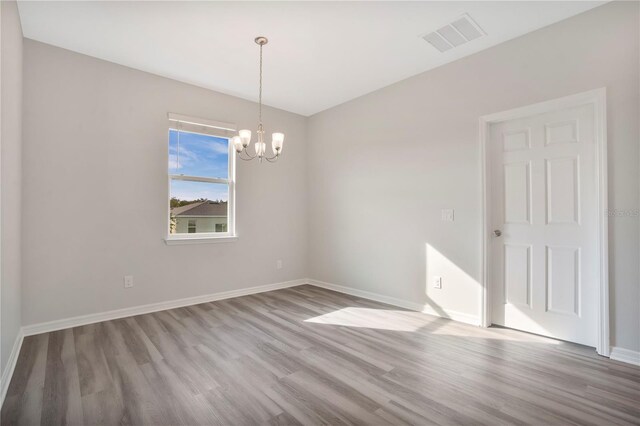 empty room with light hardwood / wood-style flooring and an inviting chandelier