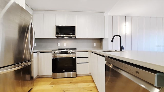 kitchen featuring stainless steel appliances, white cabinets, sink, and light wood-type flooring