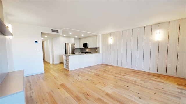 kitchen with stainless steel fridge, light wood-type flooring, sink, kitchen peninsula, and white cabinetry