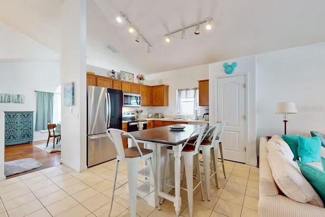 kitchen with track lighting, a center island, stainless steel appliances, lofted ceiling, and light tile patterned floors