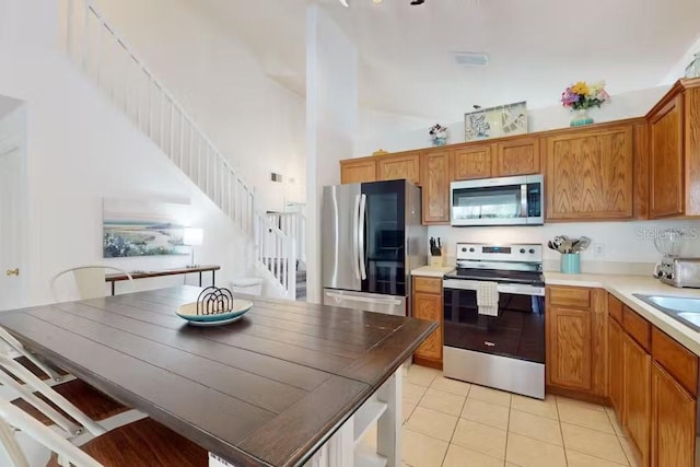 kitchen with appliances with stainless steel finishes, light tile patterned floors, and a high ceiling