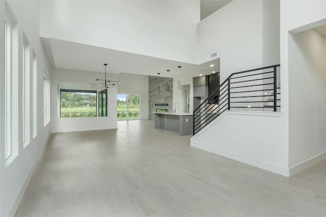 unfurnished living room featuring sink, a chandelier, a towering ceiling, and light tile patterned floors