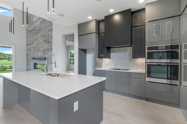 kitchen featuring stainless steel double oven, wall chimney range hood, backsplash, sink, and gray cabinets