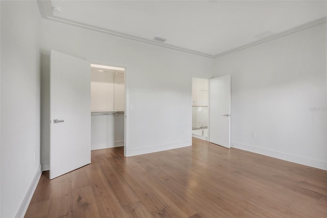 unfurnished bedroom with ornamental molding, a walk in closet, hardwood / wood-style flooring, and a closet