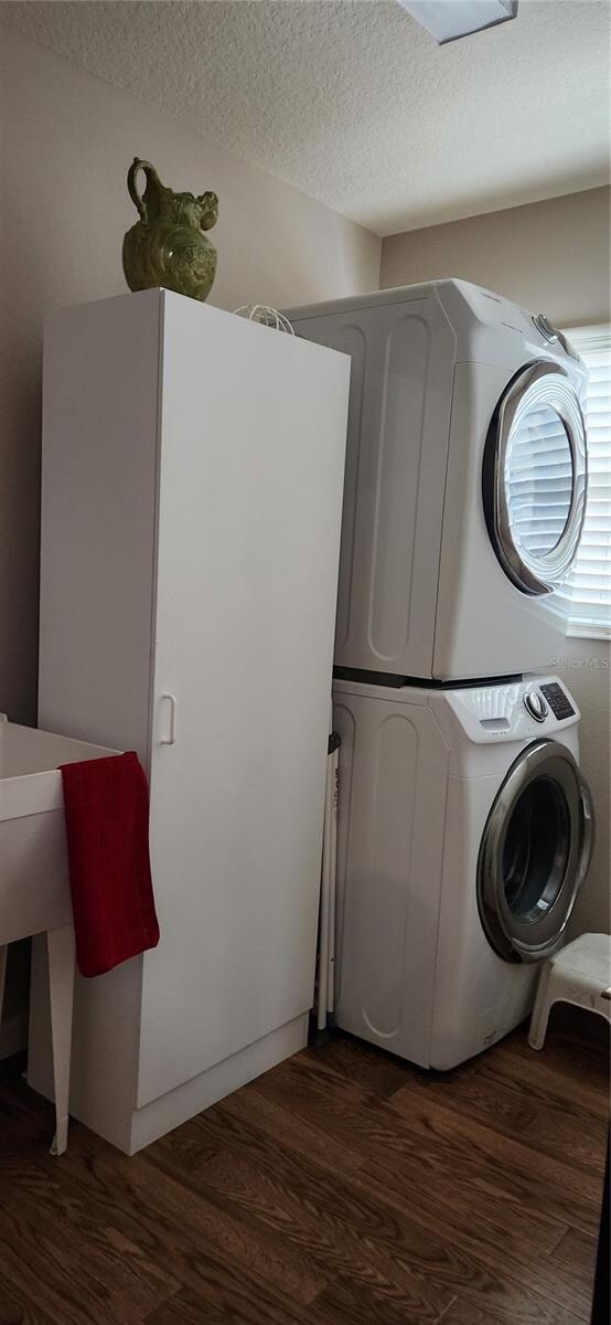 clothes washing area featuring a textured ceiling, stacked washer and clothes dryer, and dark hardwood / wood-style floors