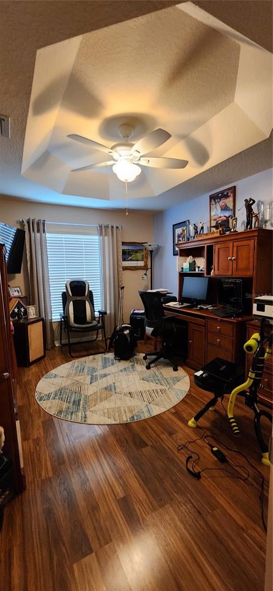 home office featuring a textured ceiling, ceiling fan, dark hardwood / wood-style floors, and a raised ceiling