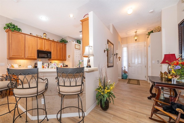 kitchen featuring light hardwood / wood-style floors, tasteful backsplash, a kitchen breakfast bar, kitchen peninsula, and a textured ceiling