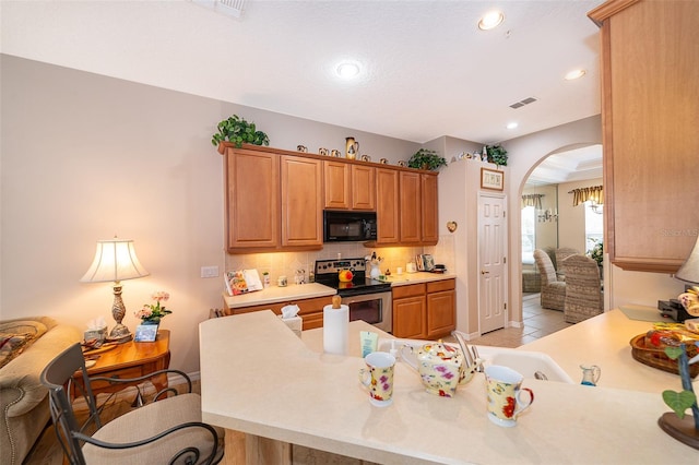 kitchen with tasteful backsplash, kitchen peninsula, a breakfast bar area, light tile patterned floors, and electric range