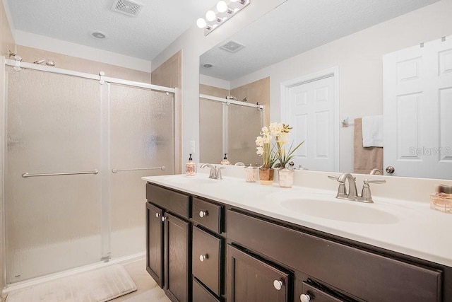 bathroom with tile patterned flooring, vanity, a shower with shower door, and a textured ceiling