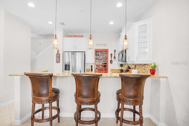 kitchen featuring light stone counters, a peninsula, stainless steel appliances, white cabinetry, and backsplash