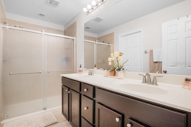 full bath featuring a textured ceiling, a sink, visible vents, and a shower stall