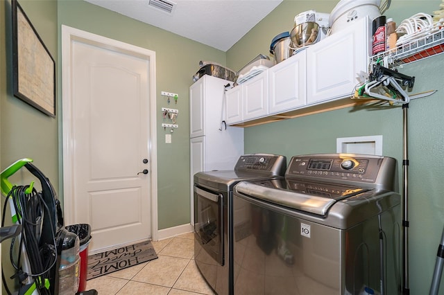 laundry area featuring washer and clothes dryer, cabinets, light tile patterned floors, and a textured ceiling