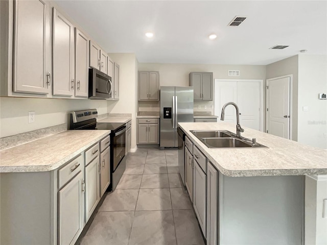 kitchen featuring gray cabinets, sink, stainless steel appliances, an island with sink, and light tile patterned floors