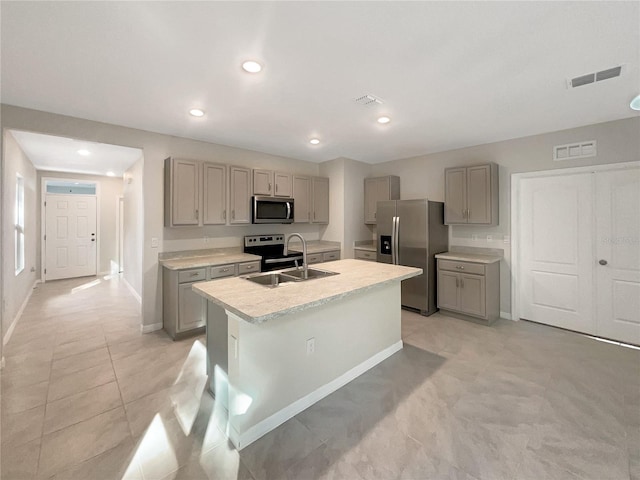 kitchen featuring an island with sink, stainless steel appliances, sink, and gray cabinetry