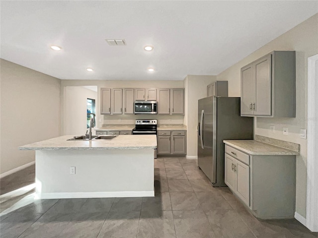 kitchen with a kitchen island with sink, gray cabinetry, sink, appliances with stainless steel finishes, and light tile patterned floors