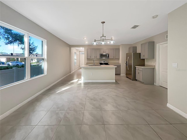 kitchen featuring hanging light fixtures, light tile patterned floors, a center island with sink, gray cabinets, and stainless steel appliances