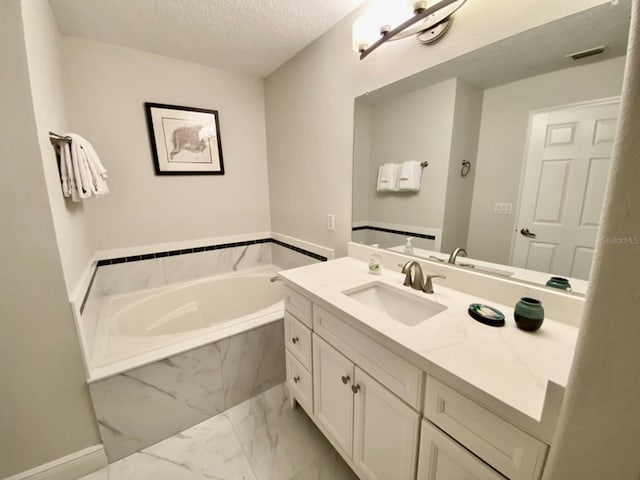 bathroom featuring vanity, a textured ceiling, and tiled tub