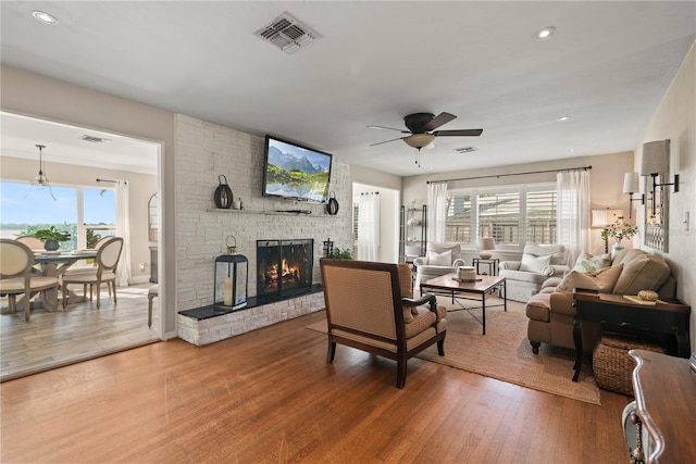 living room with ceiling fan, a brick fireplace, plenty of natural light, and hardwood / wood-style floors