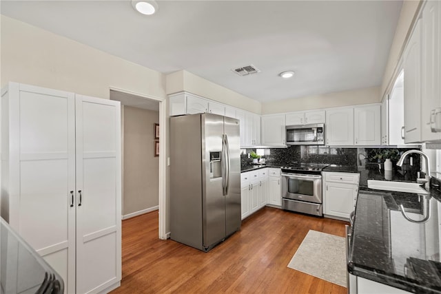 kitchen featuring dark hardwood / wood-style flooring, appliances with stainless steel finishes, white cabinetry, dark stone countertops, and sink