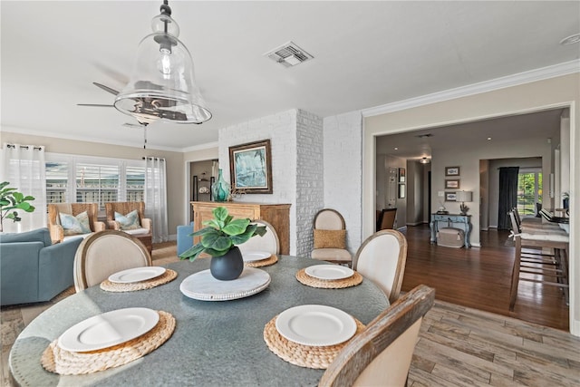 dining area with a healthy amount of sunlight, wood-type flooring, ornamental molding, and ceiling fan with notable chandelier