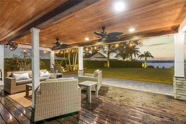 deck at dusk featuring an outdoor living space, a water view, a lawn, and ceiling fan