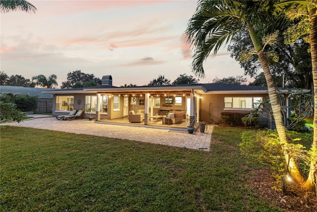 back house at dusk featuring a yard and a patio area