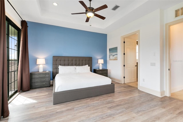 bedroom with ceiling fan, a tray ceiling, and light wood-type flooring