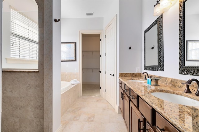 bathroom with vanity, tiled tub, and a healthy amount of sunlight