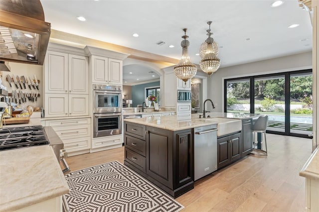 kitchen with hanging light fixtures, appliances with stainless steel finishes, light wood-type flooring, range hood, and sink