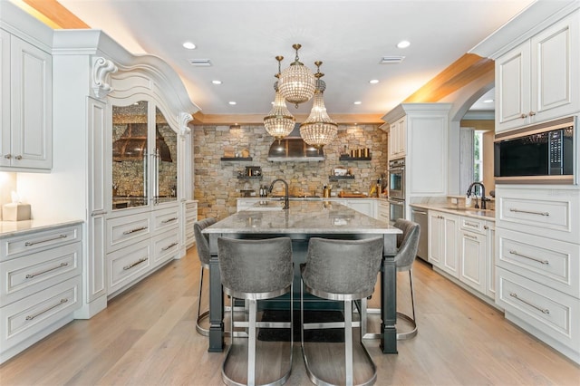 kitchen with an island with sink, hanging light fixtures, black microwave, sink, and white cabinetry