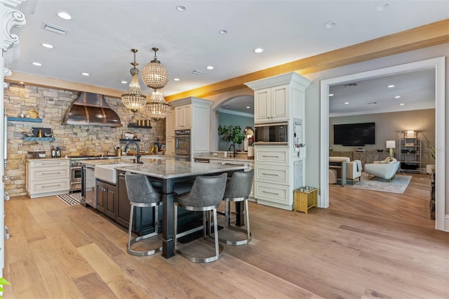 kitchen featuring wall chimney range hood, white cabinets, a breakfast bar, light hardwood / wood-style floors, and stainless steel appliances