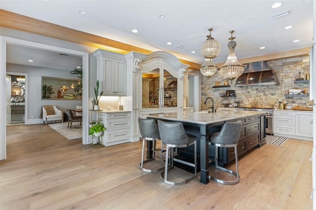 kitchen with light hardwood / wood-style floors, wall chimney range hood, backsplash, and a center island with sink